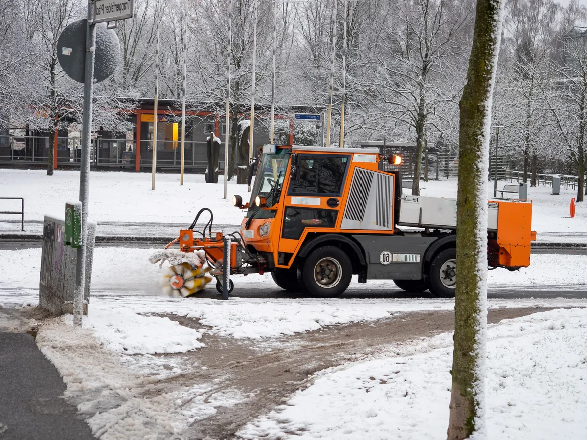 Kommunales Winterdienstfahrzeug mit Kehrbesen räumt Schnee auf einer Verkehrsfläche